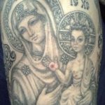 Фото тату Богоматери с младенцем в круге, выполненное в черно-серых тонах. Изображение размещено на плече и отличается традиционной иконографией.