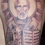 Фото татуировки с изображением Николая Чудотворца, выполненной в реалистичном стиле с использованием оттенков серого и черного.