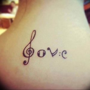 Фото тату на шее: надпись "love", объединенная со скрипичным ключом. Простой и элегантный черно-белый рисунок татуировки.