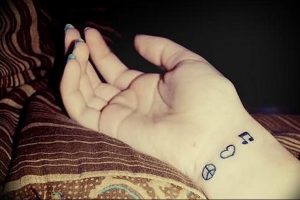 Фото тату на руке: три небольших символа - нота, сердце и символ мира. Минималистичный рисунок татуировки в черном цвете.