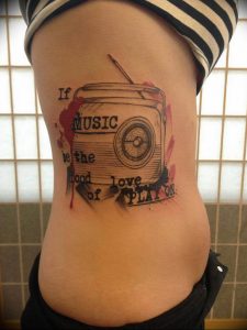 Фото тату на боку: старинное радио с надписью 'MUSIC be the sound of love PLAY ON'. Яркий рисунок татуировки с элементами акварели.