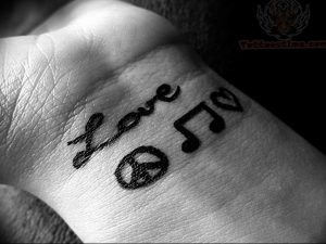 Фото тату на запястье с надписью 'love', музыкальной нотой и символом мира. Простой и символичный рисунок татуировки.
