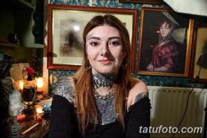 Фотография мастера тату, молодой женщины, в уютной тату-студии. Она позирует на фоне картин и инструментов для татуировки.