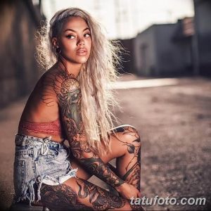 Фотография девушки с множеством татуировок в стиле ориентал на руках и ногах. Она позирует в непринужденной обстановке, демонстрируя свои татуировки.