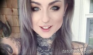 Фотография девушки с длинными серыми волосами и сложной татуировкой на шее и плече. Татуировка выполнена в черно-белой гамме и имеет детализированный рисунок.