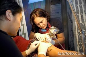 Фото процесса нанесения татуировки: мастер в перчатках наносит рисунок на руку клиента, используя тату-машинку.