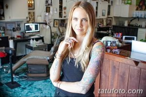 Фото тату-мастера в студии: девушка с татуировками на руках стоит за стойкой, демонстрируя свои работы.