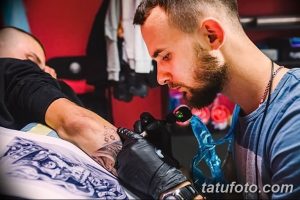 Фотография мастера тату, работающего над татуировкой на руке клиента. Подчеркивает точность и мастерство.