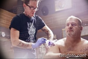 Фотография процесса нанесения татуировки: мастер в перчатках работает над рисунком на теле клиента.