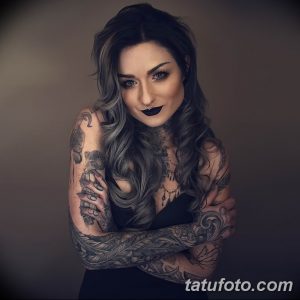Фотография девушки с длинными серыми волосами, покрытой сложными татуировками в стиле реализм и графика. Тату покрывают руки, плечи и шею.
