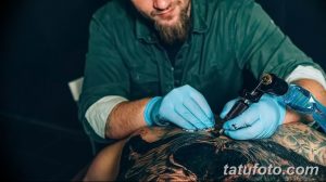 Фото тату процесса нанесения татуировки опытным мастером. Видны руки мастера в голубых перчатках, тату-машинка и кожа клиента.