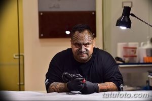 Мастер тату с традиционными татуировками на лице и руках, держащий тату-машинку.