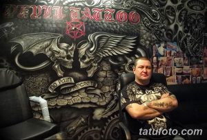 Фото тату-салона с мастером тату. Виден мастер, сидящий в кресле перед стеной с татуировками и рисунками.