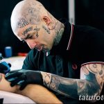 Фото тату процесса нанесения татуировки опытным мастером. Виден мастер с татуировками на теле, работающий с тату-аппаратом над рисунком на клиенте.