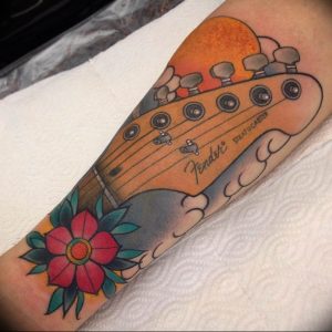 Фото тату на предплечье с изображением грифа гитары Fender Stratocaster и красной розы в стиле олдскул.