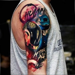 Яркая и красочная татуировка на плече с изображением шлема Daft Punk, брызг краски и надписи 'Human After All'.