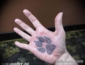 Фото тату с изображением отпечатка лапы на ладони. Черно-белый рисунок татуировки, выполненный в реалистичном стиле.