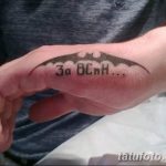 Фото тату: Изображение крыла Бэтмена и надпись 'За Всех...' на ладони. Черно-белый рисунок татуировки, выполненный в минималистичном стиле.