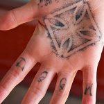 Фото тату: геометрический узор в виде ромба на ладони руки с надписью 'TATTO'. Черно-белая татуировка с тонкими линиями и минималистичным дизайном.