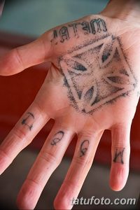 Фото тату: геометрический узор в виде ромба на ладони руки с надписью 'TATTO'. Черно-белая татуировка с тонкими линиями и минималистичным дизайном.