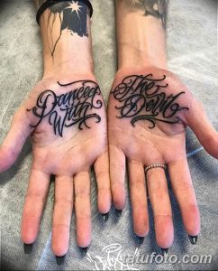 Фото тату надписи "Dance With The Devil" на обеих ладонях. Рисунок выполнен в каллиграфическом стиле, с использованием черных чернил.