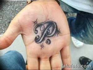 Фото татуировки на ладони с изображением буквы 'P', украшенной узорами и звездочками. Черно-белый рисунок.