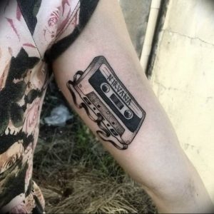 Фото тату: черно-белый рисунок кассеты с логотипом Nirvana на предплечье. Стиль - минимализм, четкие линии.