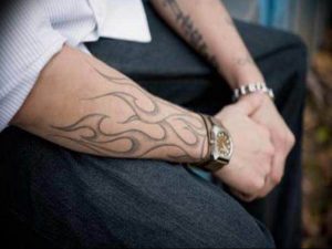 Фото тату в стиле tribal, изображающего языки пламени, обвивающие предплечье. Черно-серый рисунок с плавными линиями и динамичной композицией.