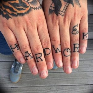 Фото тату: надпись 'HARD WORK' татуирована на фалангах пальцев. Черные буквы, минималистичный дизайн.