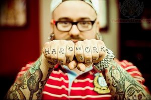 Фото тату: мужчина с татуировками на руках, на которых надпись 'HARD WORK' на костяшках пальцев и различные рисунки.