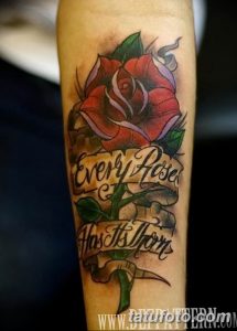Фото тату красной розы с надписью 'Every Rose Has Its Thorn' на предплечье. Классический стиль татуировки с яркими цветами и четкими линиями.