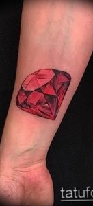 Фото тату рубинового осколка на запястье. Небольшой, но яркий рисунок драгоценного камня.
