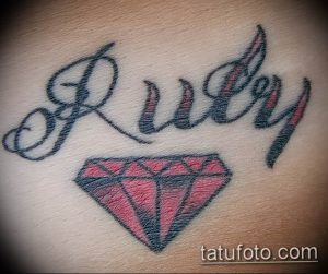 Фото тату рубина и надписи 'Ruby' выполненной каллиграфическим шрифтом. Минималистичный рисунок татуировки в черных и красных тонах.