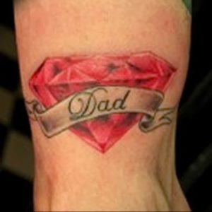 Фото тату на руке с изображением красного бриллианта и надписи "Dad". Реалистичный стиль, яркие цвета, посвящение отцу.