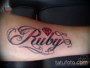 Фото тату на руке с надписью 'Ruby' и изображением бриллианта. Элегантный шрифт и детализированный рисунок создают женственный образ.