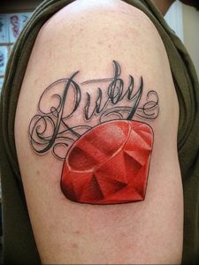 Фото тату рубина на плече с надписью 'Ruby'. Реалистичное изображение драгоценного камня с яркими красными оттенками.