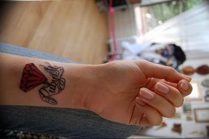 Фото миниатюрной татуировки на запястье с надписью 'Forever' и красным бриллиантом. Татуировка выполнена в черном и красном цветах.