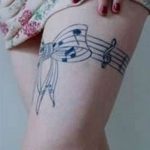 Фото тату: изящная татуировка на боку с изображением нот, скрипичного ключа и музыкальных линий. Черно-белый рисунок выглядит легко и воздушно.