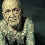 Фото пожилого мужчины, покрытого татуировками в традиционном стиле. Татуировки рассказывают историю его жизни, отражая его опыт и убеждения.