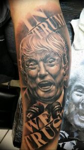 Фотография татуировки с реалистичным портретом Дональда Трампа на руке мужчины. Под портретом надпись 'We Trust'.