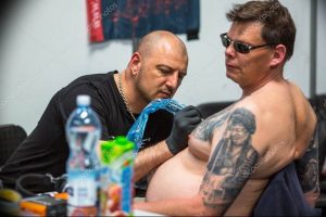 Фото процесса татуировки: мастер тату делает татуировку мужчине на спине. Видны инструменты, чернила и кожа клиента.