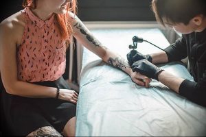 Фотография процесса нанесения татуировки на руку девушки. Видна рука мастера с тату-машинкой и рука клиента.