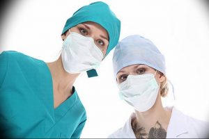 Фото двух медсестер в медицинских масках и шапочках, одна из которых имеет татуировку на шее.