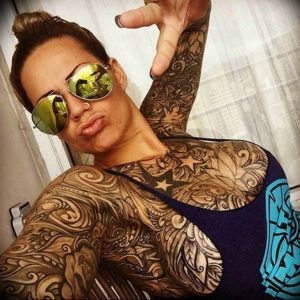 Фотография женщины с татуировкой в стиле blackwork, покрывающей ее плечи, грудь и руки, демонстрирующая сложный и детализированный рисунок татуировки.