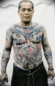 Фотография пожилого мужчины с масштабной татуировкой в японском стиле, покрывающей его тело, демонстрирующая сложный и детализированный рисунок татуировки.