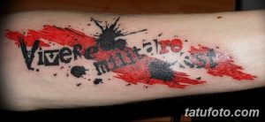 Фото тату на руке: надпись 'Vivere Militare Mori' в стиле граффити, выполненная красными и черными чернилами с брызгами.