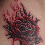 Фото тату: Красная роза с черными листьями и капельками крови на коже. Готический рисунок татуировки с драматичным эффектом.