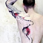 Фото тату: абстрактный рисунок на спине мужчины, выполненный в технике брызг краски, сочетающий черный, серый и красный цвета.