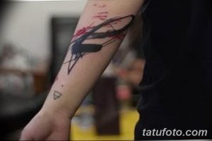 Фото тату на руке: абстрактный рисунок, имитирующий мазки кистью и брызги краски. Минималистичная татуировка в черном и красном цветах.