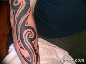 Фото тату в стиле трайбл на предплечье, выполненной в черных тонах с использованием плавных линий и спиралей.